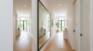 A bright, modern narrow hallway featuring a large, statement floor-to-ceiling mirror that reflects l